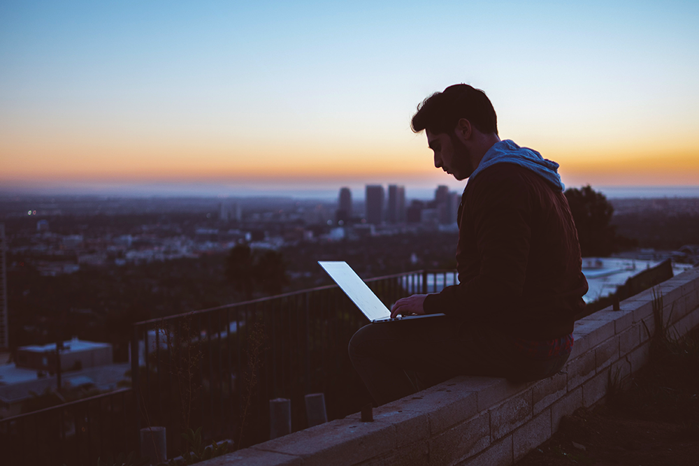 A person sitting of the roof with their computer.