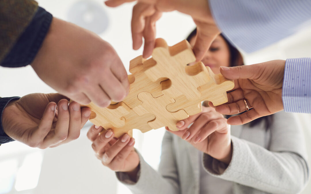 Business people holding wooden puzzle pieces in their hands and connect at a business meeting in the office. Concept of teamwork.