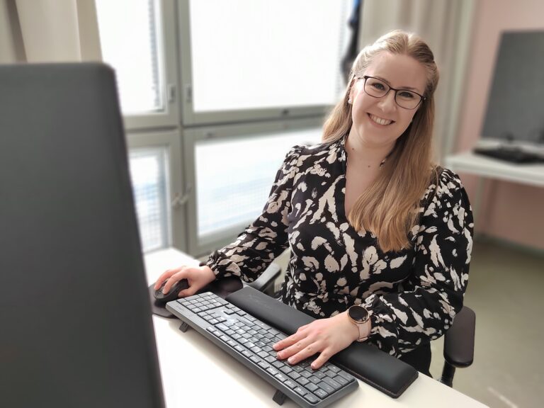 Hymyilevä Johanna Kivimäki työpöytänsä ääressä