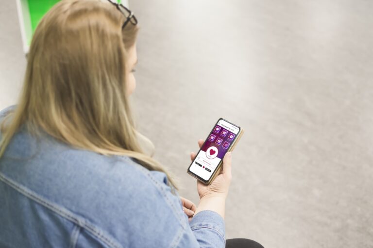 Naisopiskelija on selkä kohti kameraa ja katsoo puhelintaan, jossa on auki Tuudon Rekrymessujen näkymä