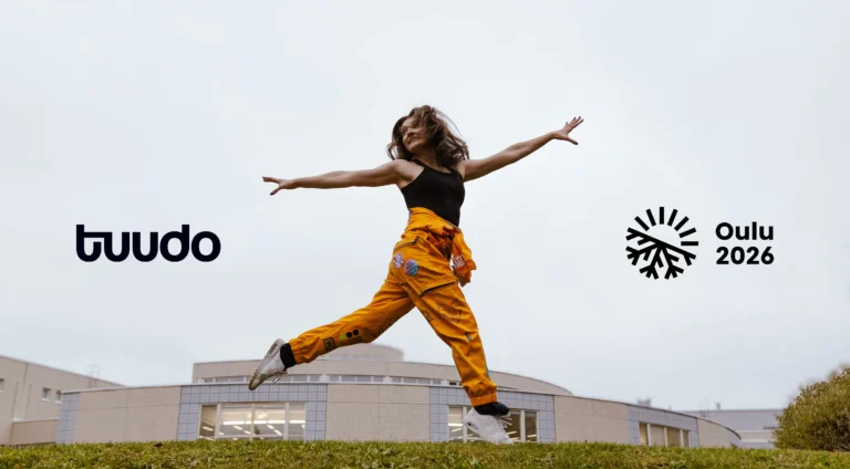 Tuudo ja Oulu2026 -logot taivaalla, edessä opiskelijanainen keltaisissa haalareissa.